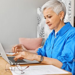 People, job, occupation, age and employment. Indoor image of beautiful gray haired female on retirement looking for remote work using portable computer. Mature woman photographer typing on laptop
