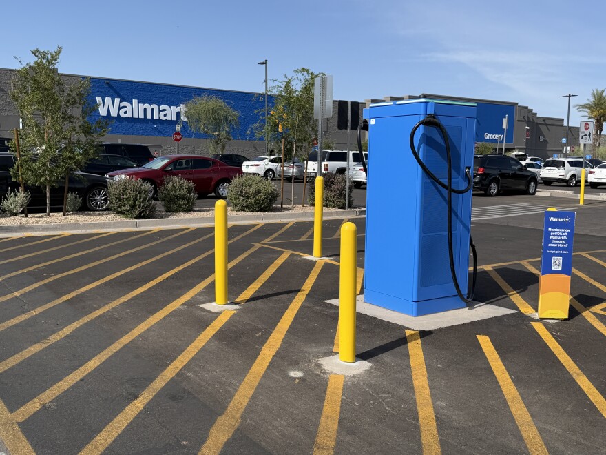 An outdoor daytime photograph shows a bright blue electric vehicle charging station the parking lot in front of a Walmart store.