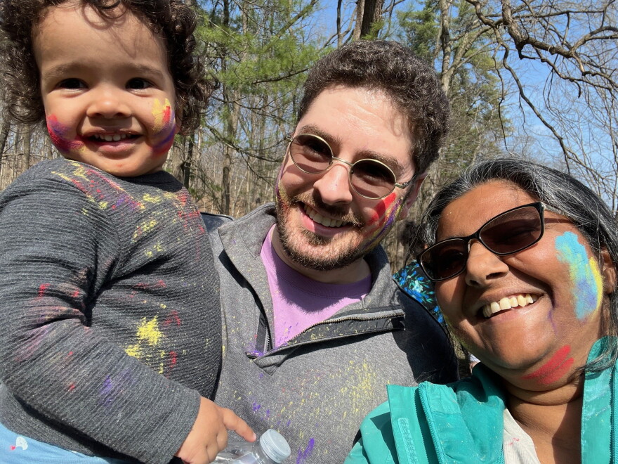 A man and woman pose with a child. All three have paint splattered on parts of their face.