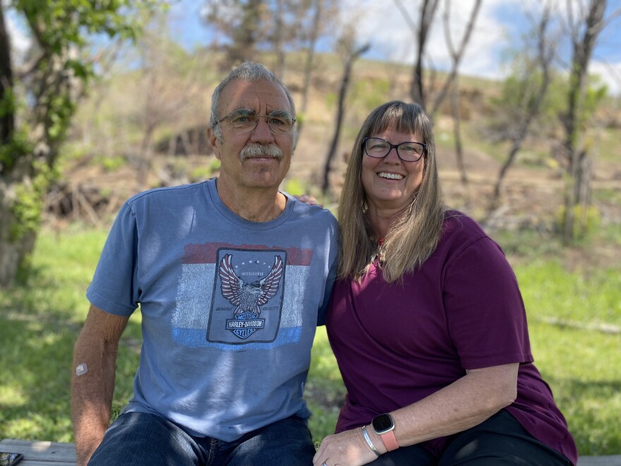 Bob and Diana Gabriella sit by a small creek on their property in the tiny community of Marshall, in unincorporated Boulder County. They hope to rebuild two of the ten buildings they lost in the Marshall Fire but are facing a variety of delays.
