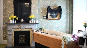 A wooden coffin sits below a portrait draped in black