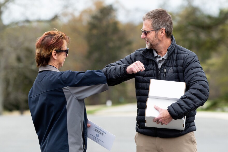 Ivar Lonon bumps elbows with Sonya Leazer, a representative at Salisbury National Cemetery, while holding boxes containing the cremated remains of his mother and father in Salisbury, N.C., on Thursday, March 26, 2020.