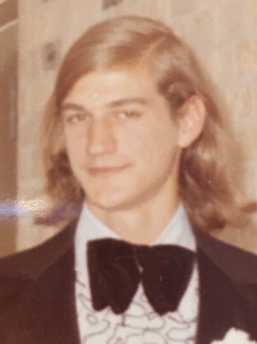 A photo of a young man with long blond hair in a suit and bow-tie