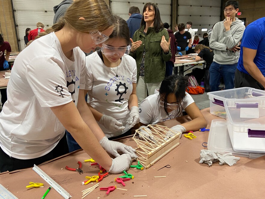 A team of three female students build a miniature bridge.