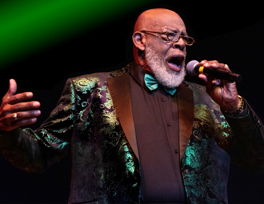 A man in a green jacket sings into a microphone.