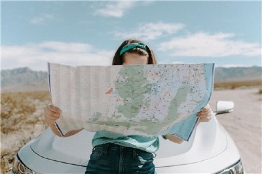 A woman reads a map in front of a car. 