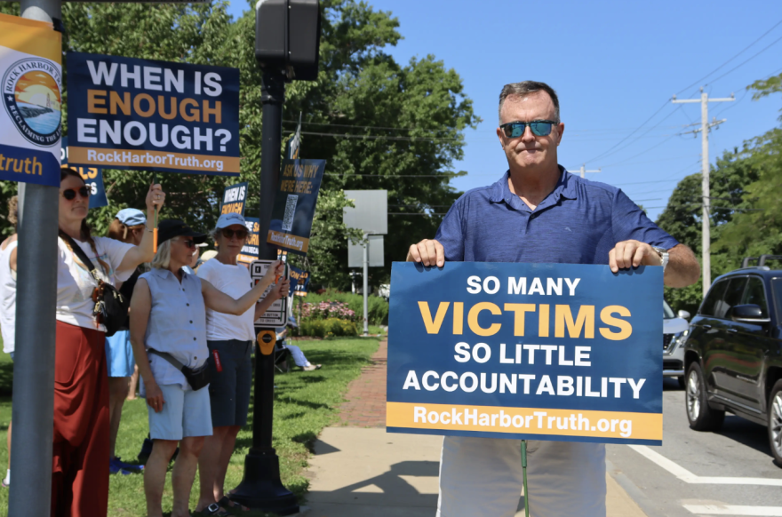Shawn DeLude holds a sign at a gathering of former Community of Jesus residents and their supporters in August of 2026 in Orleans.