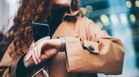 A woman checks her watch while holding a smartphone. (Maria Korneeva/Getty Images)