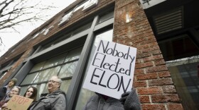 A person protesting Elon Musk's actions in the Trump administration holds a sign outside a Tesla showroom in Seattle on Thursday, Feb. 13, 2025. (AP Photo/Manuel Valdes)