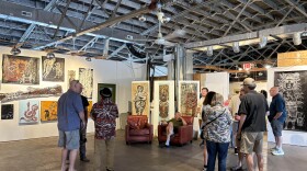 people standing around in a spacious art gallery with paintings on the walls and exposed trusses and duct work