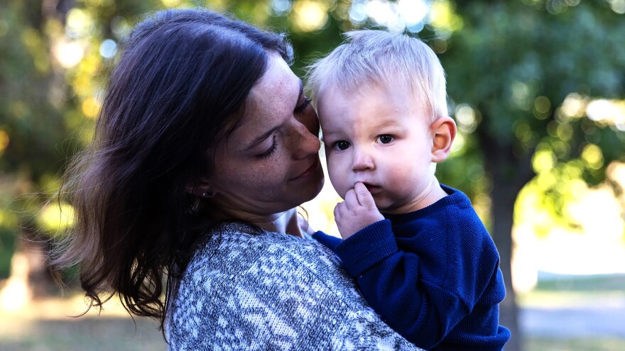 Woman with loving look on her face holds a toddler boy with blond hair in her arms 
