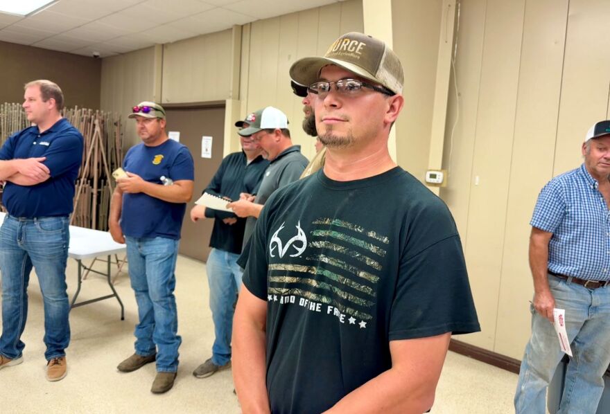 A young man with glasses and a ball cap is standing in the back of a land auction.