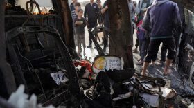 People gather around the wreckage of a car used by US-based aid group World Central Kitchen, that was hit by an Israeli strike the previous day in Deir al-Balah in the central Gaza Strip amid the ongoing battles between Israel and the Palestinian militant group Hamas.