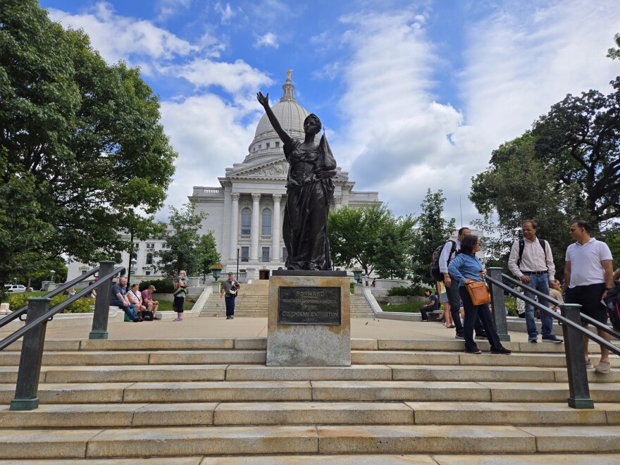 A picture of the Wisconsin Capitol and the "Forward" statue in front of it, a bronze allegorical figure of a woman symbolizing progress, created by Jean Pond Miner for the 1893 World's Fair, representing women's suffrage and the state's motto.