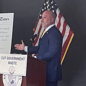 Florida CFO Blaise Ingoglia stands at a poduim that has a sign with the words "Cut Government Waste" hanging from it