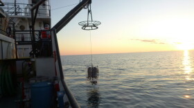 A sampling unit is lowered into the water off the side of a ship.