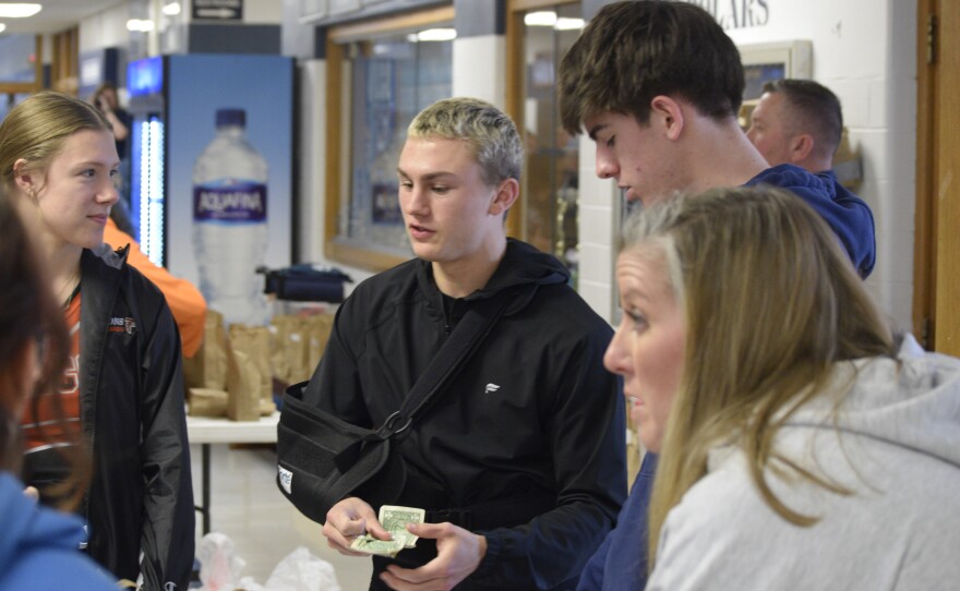 Zane Hoffman, center, stands at the hockey puck table. Without being able to charge for admission to the game, students could spend a dollar to buy a hockey puck. These pucks were thrown at halftime of the boys game, with whomever could hit a bull’s eye placed on the court winning $25.