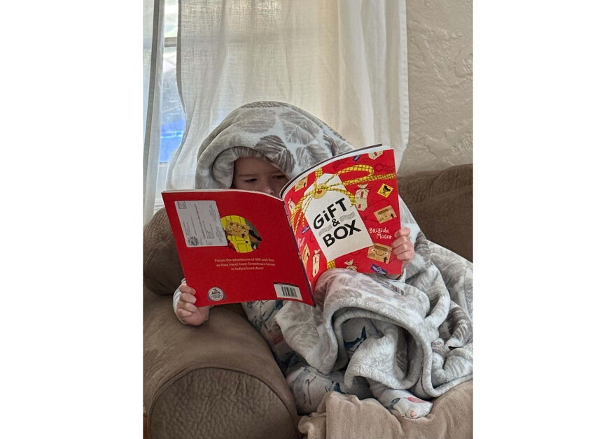 Bjorn Alder reads "Gift & Box" by Ellen Mayer while snuggled in a blanket.