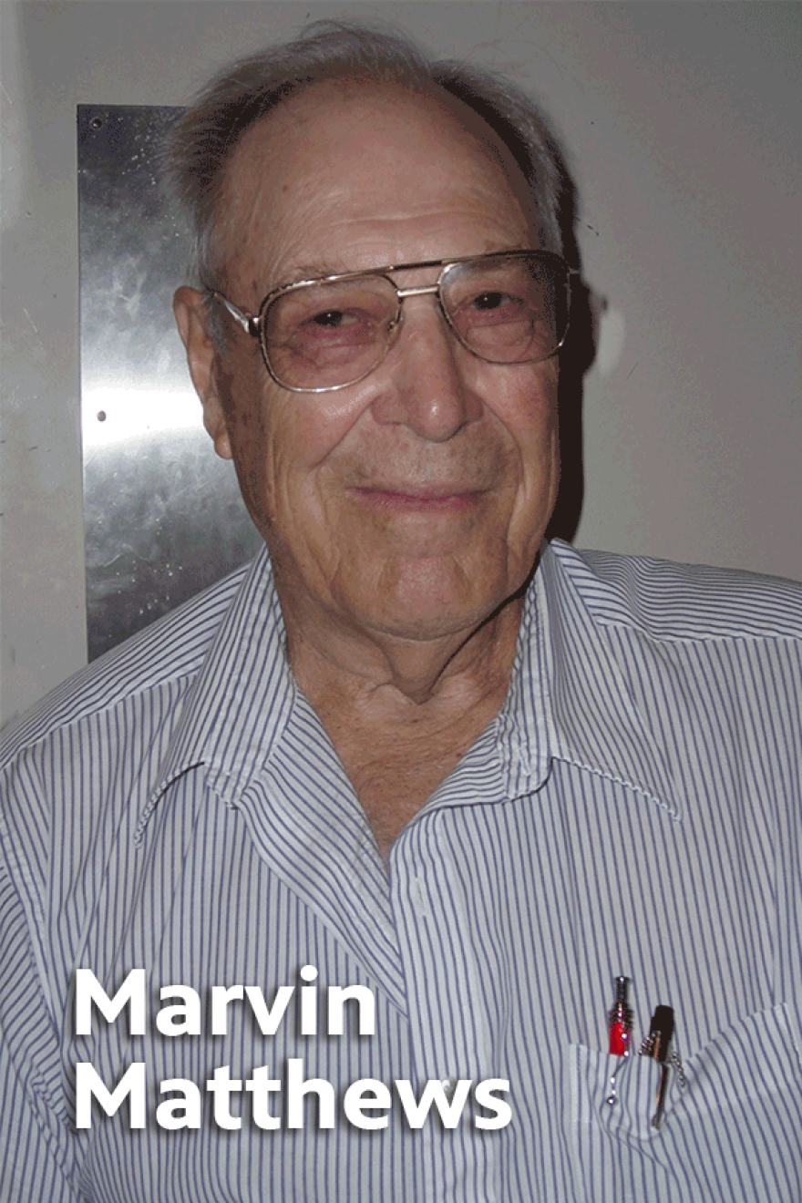 Elderly Marvin Matthews wearing glasses and gray and white pin stripe button-up shirt