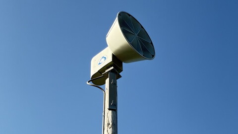 a siren on top of a light pole with blue sky behind it