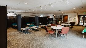 A room is filled with cots that are divided by curtains. There are several tables scattered around the room that have games on them.