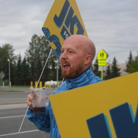 Gubernatorial candidate Jonathan Kreiss-Tomkins hoists a campaign sign on the morning of Aug. 18, 2026, Alaska’s primary election day.