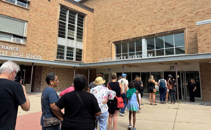 A line forms out front of a high school building. 