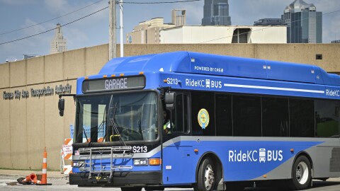 Exterior photo of a blue transit bus entering the street from a parking lot. Behind it is a building with a sigh that reads "Kansas City Area Transportation Authority."