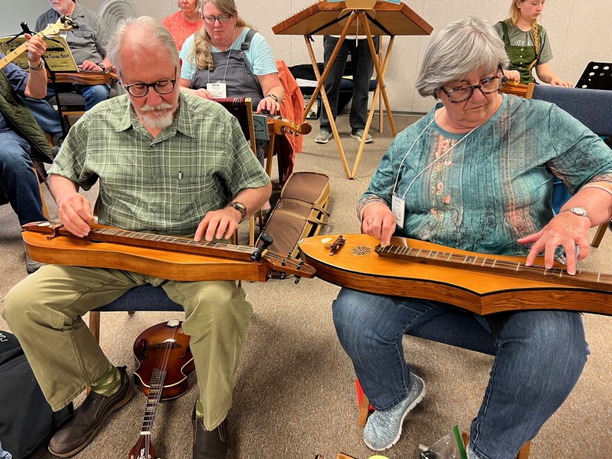 Two musicians balance dulcimers on their laps as they strum.