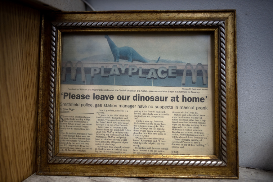 A newspaper article titled "'Please leave our dinosaur at home'" with a picture of a dinosaur on the roof of a McDonald's.