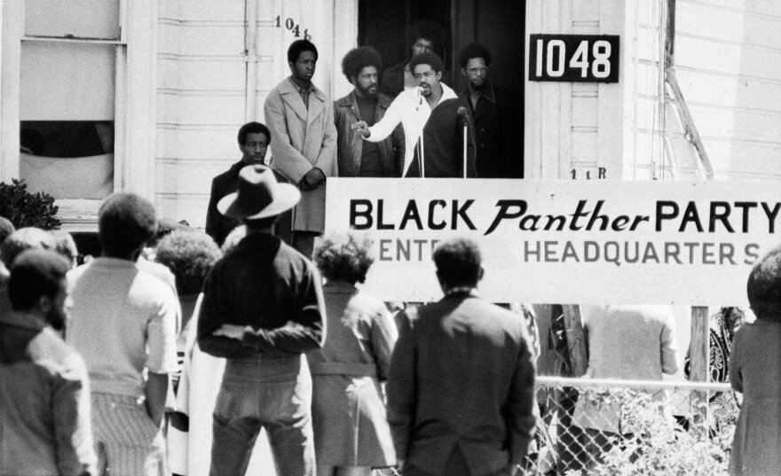 A black and white photo of people on steps and people looking at the people on the steps. There's a sign that reads black panther party headquarters