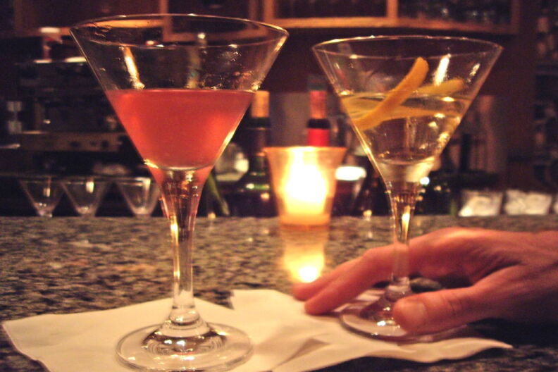 Two cocktails sit on a bar.