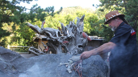 A man holds a burning piece of sage in a secluded garden memorial. 