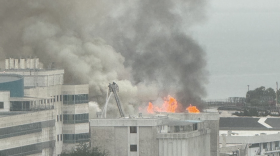 multiple buildings with flames and large plume of gray smoke coming from one of the buildings 