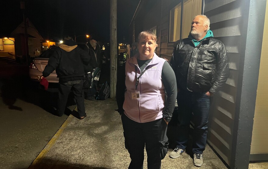 A man and woman stand in front of a building at night. 