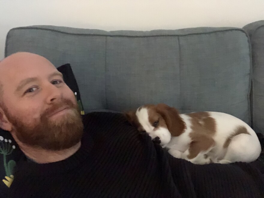 Bearded man lying on a couch with a puppy curled up asleep on his chest