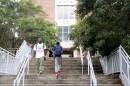  Two students walk down a long staircase. In back of them is a brick, campus building