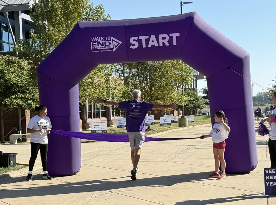 man with outstretched arms in purple shirt crossing finish line of Alzheimer's Association walk