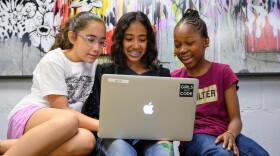 Three girls are looking at a laptop.