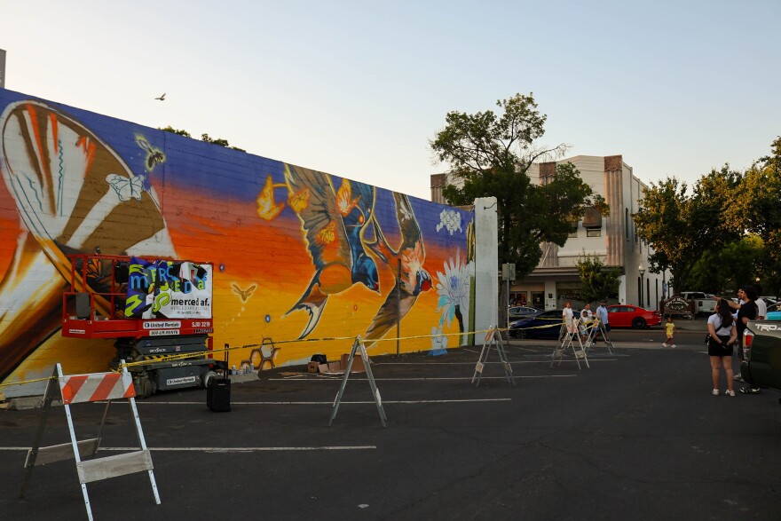 Spectators look at Joel Aguilar’s portion of the mural in progress on Thursday, May 21st.