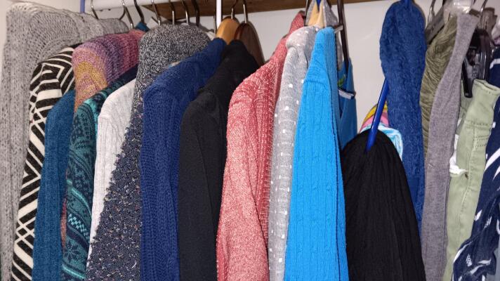 A variety of sweaters and pants hang on hangers in a closet. 