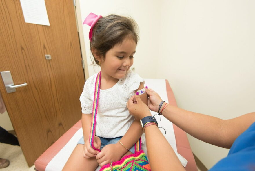 A health care worker places a bandage on a child after giving a vaccination shot. New federal guidance to reduce the number of recommended childhood vaccines from 17 to 11 comes as states including Florida are already charting their own course on vaccine policy.