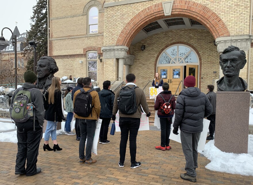 A small group of students standing outside Old Main building at USU holding signs, with one person on the steps talking to the group.