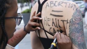 woman writing "abortion = health care" on another woman's back