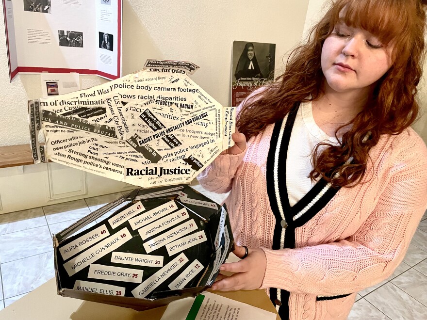 Claire Miller holds her casket open, displaying the inside which is covered in newspaper clippings from instances of racial injustice and, on the bottom, the names and ages of individuals who have been victims of police brutality.