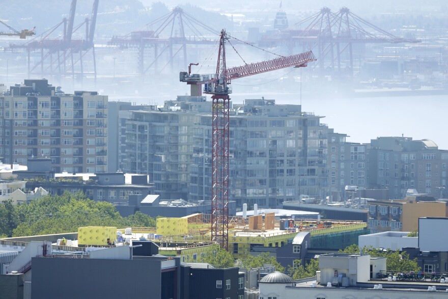 A construction crane working on a building is shown with Port of Seattle cranes in the background on a foggy summer day, Monday, July 15, 2014, in Seattle.