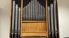 A brown and silver organ stands in front of a white wall