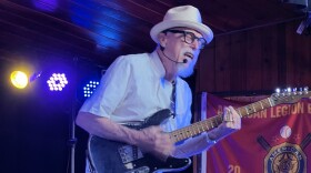 A man wearing a hat and playing an electric guitar on a stage