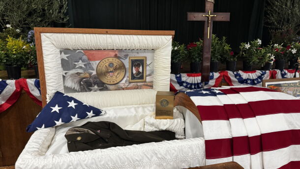 Casket with photos of Sgt. Adolph Aguirre and his uniform. American flag draped over. 