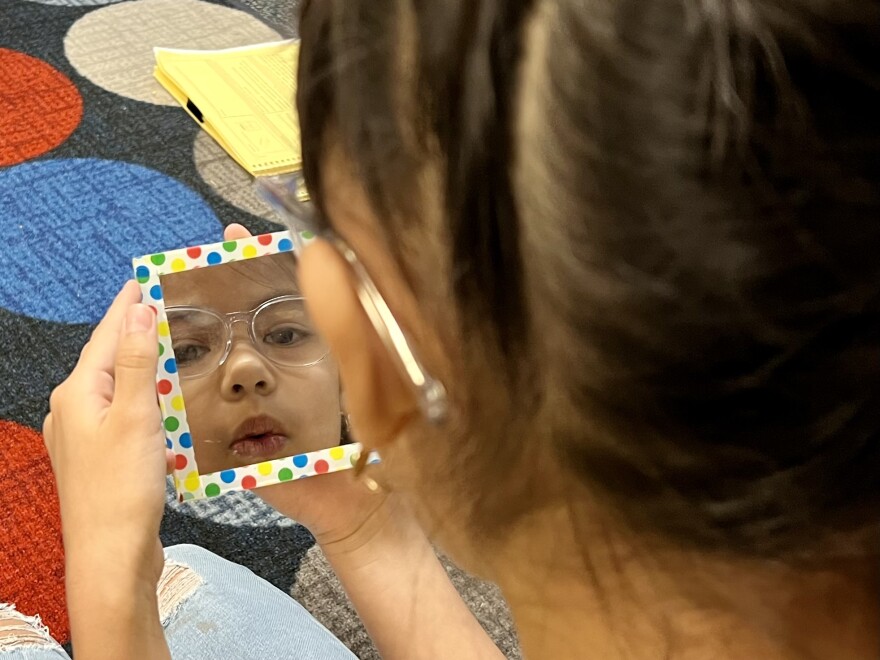 A first-grader at Washington Elementary School watches her mouth in a mirror as she makes the vowel sounds in "owl" and "how."
